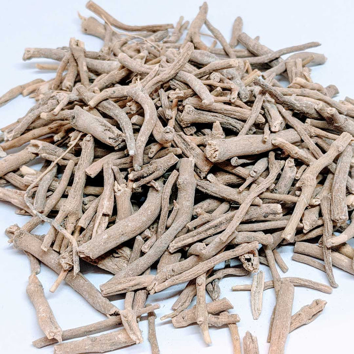 A pile of dried Ashwagandha roots, light brown in color, with rough, twig-like appearance and various lengths, scattered on a white surface.
