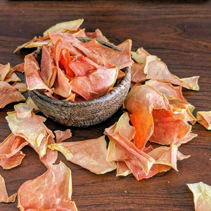 Dried papaya slices on a wooden surface with a small bowl.